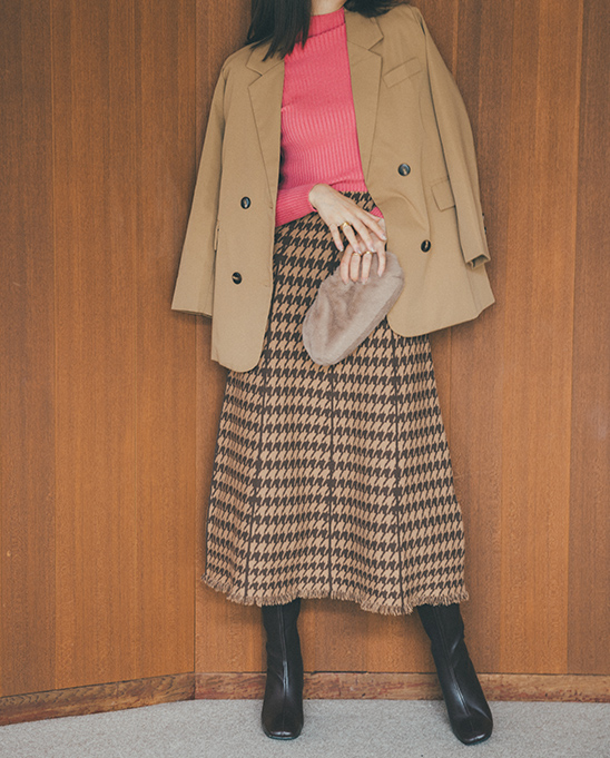 キャメルのジャケットにピンクのニットチェックのミディ丈スカートとロングブーツをコーディネートした女性の画像