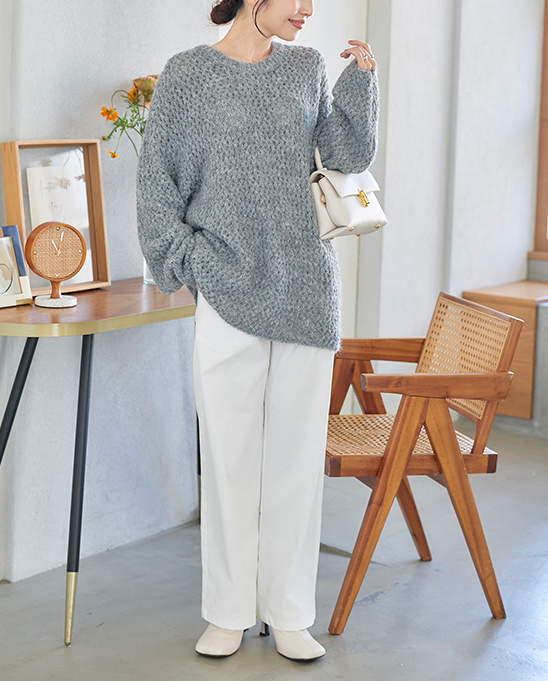 グレーのざっくり編みニットに白のワイドパンツとショートブーツをコーディネートした女性の画像