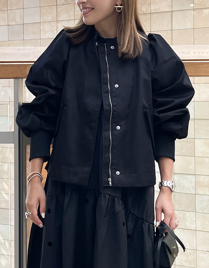 黒のノーカラーブルゾンに黒のフレアスカートをコーディネートした女性の画像