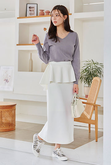 くすみラベンダーのニットに白のフリルタイトスカートを着た女性の画像