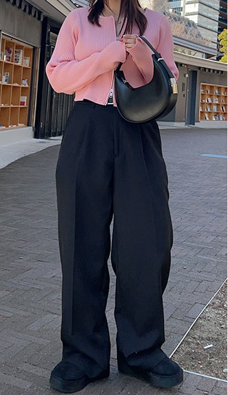 ピンクのショート丈トップスに黒のハイウエストワイドパンツを着た女性の画像